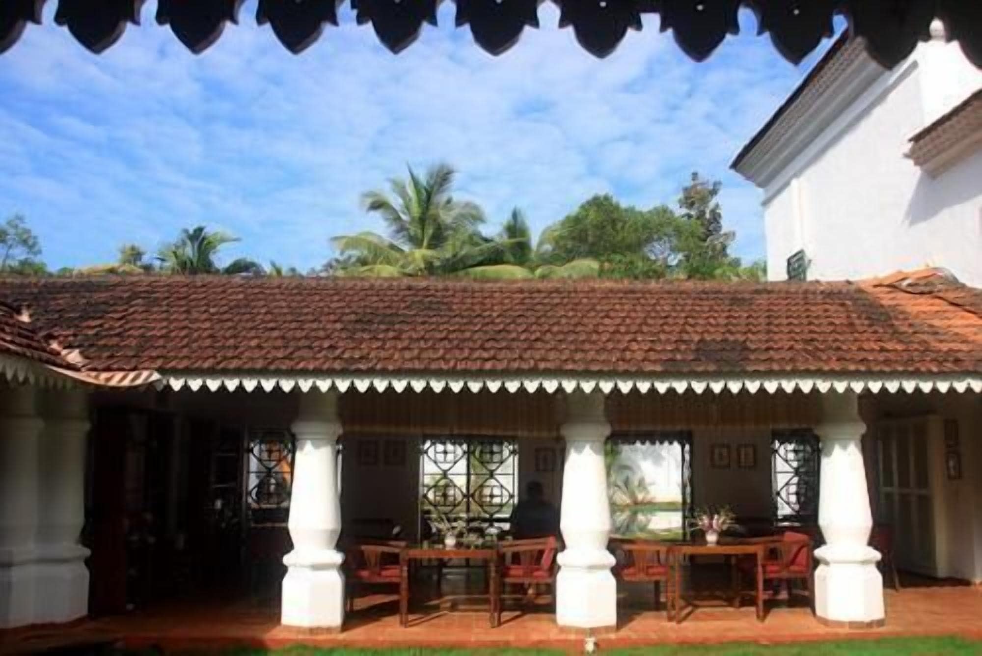 A covered outdoor area with a tiled roof, white columns, and wooden furniture.