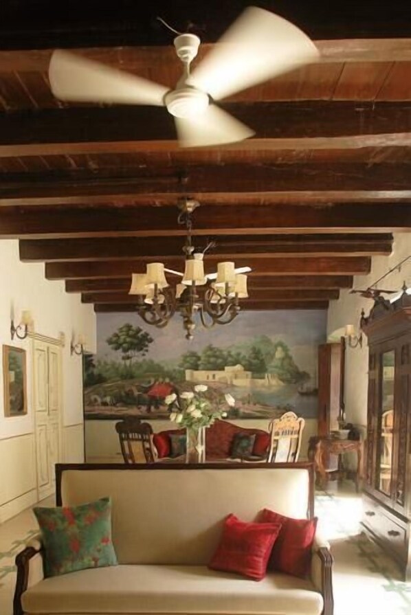 Una habitación con ventilador de techo, lámpara de araña, sofá con cojines rojos y un mural en la pared.