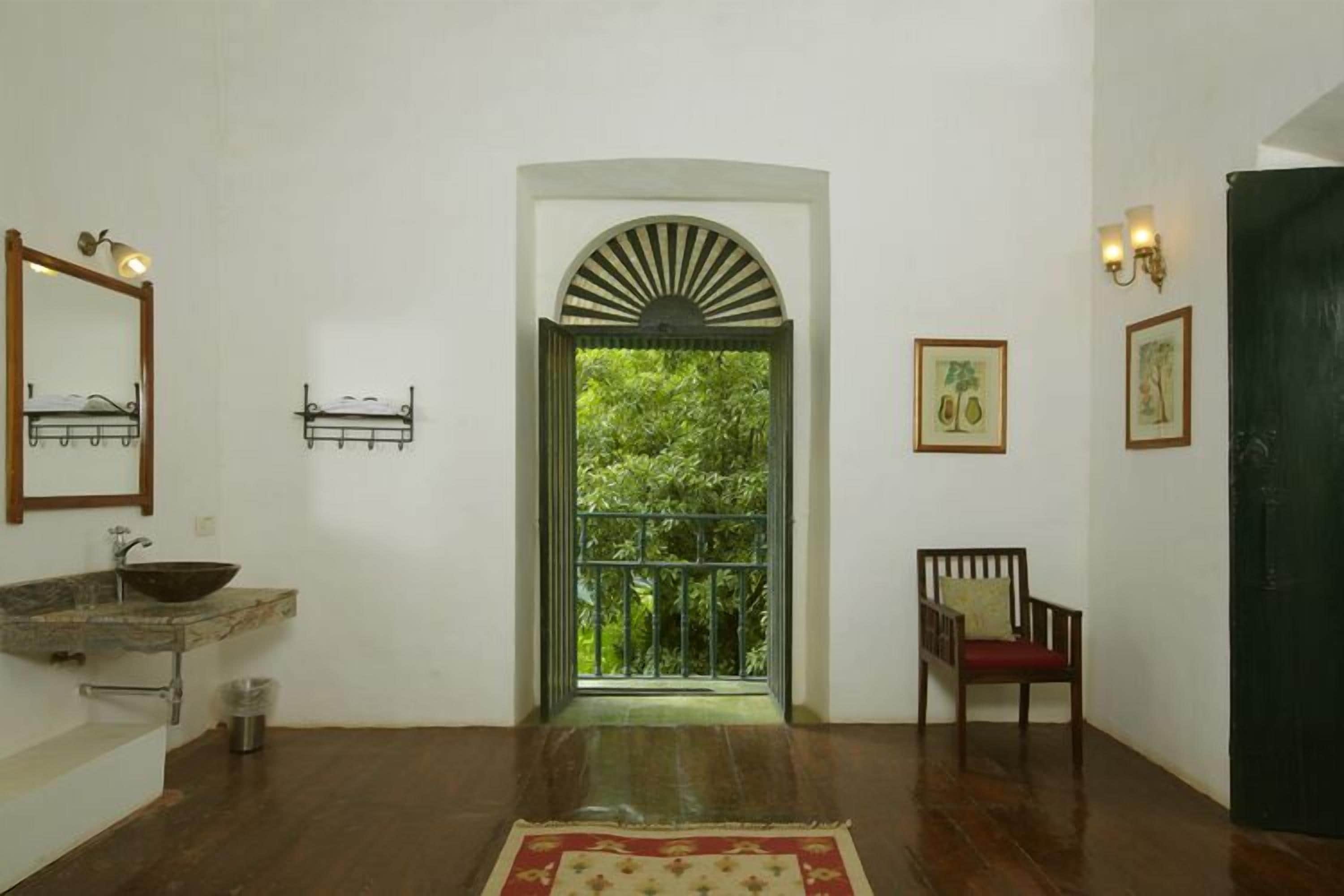 A hallway with a wooden floor, a sink, a chair, and a door leading to a balcony with greenery.