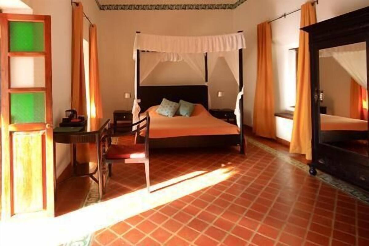 Ein Schlafzimmer mit einem Himmelbett, einem Schreibtisch mit Stuhl und einem großen Spiegel.