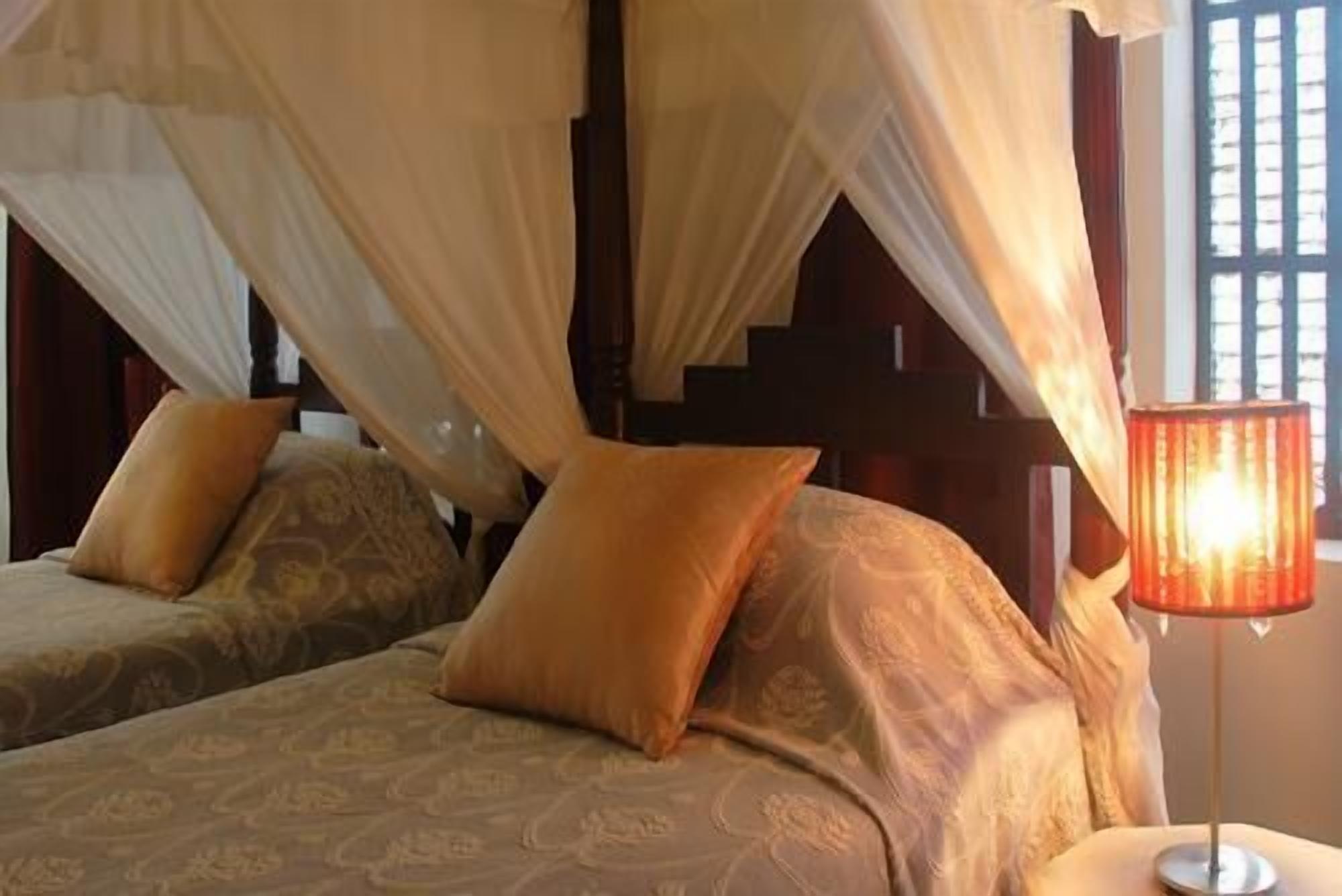 Un dormitorio con dos camas, cada una con ropa de cama y almohadas estampadas, una cama con dosel y una lámpara de noche.
