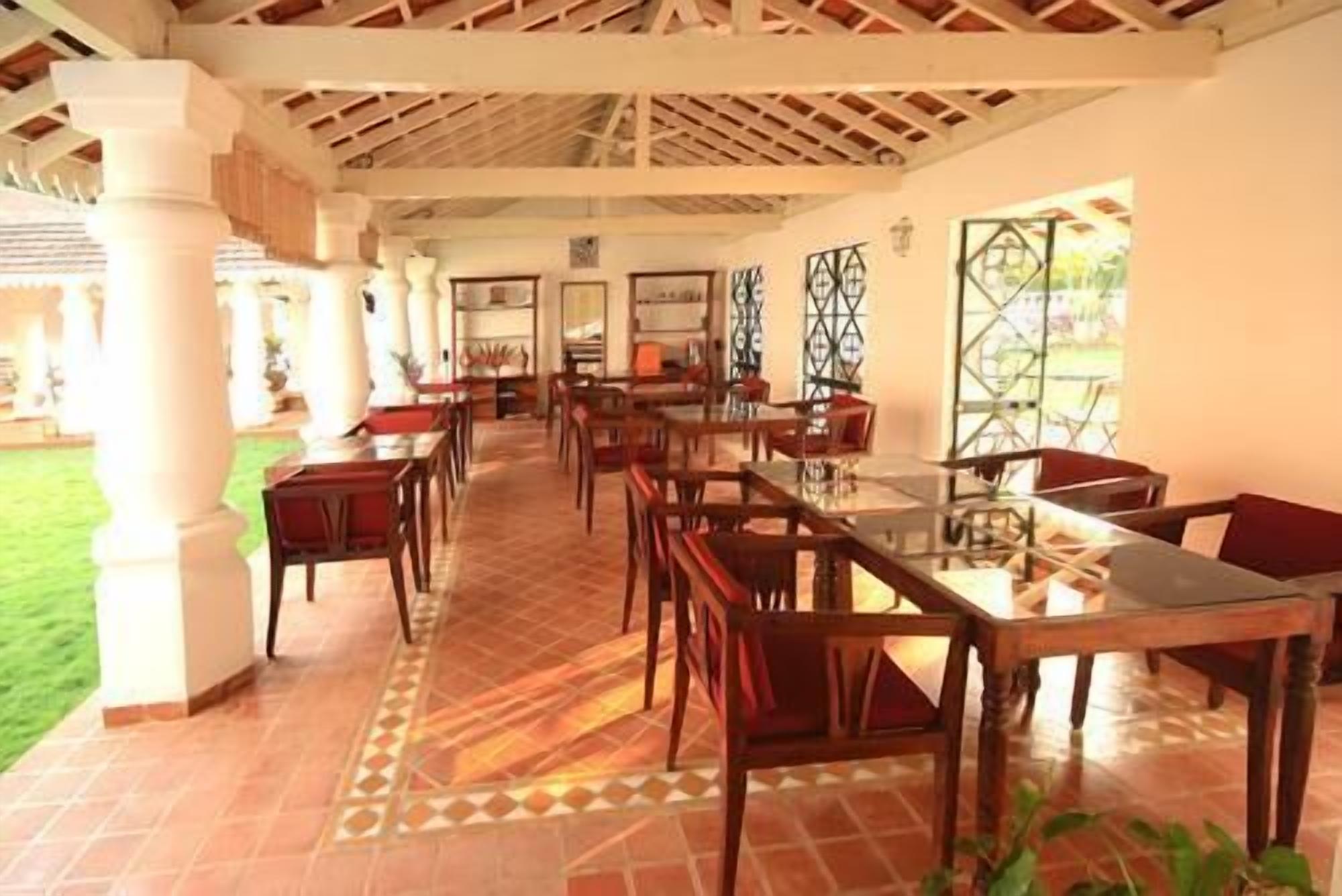 A spacious indoor dining area with multiple tables and chairs, a tiled floor, and a ceiling with wooden beams.