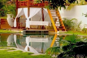 Un espace extérieur paisible, aménagé avec une table et des chaises, une terrasse en bois et dont le reflet se mire dans l’eau.