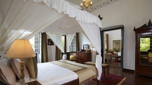 A bedroom with a canopy bed, a wooden nightstand, a lamp, and a dresser. - Siolim House (Siolim)