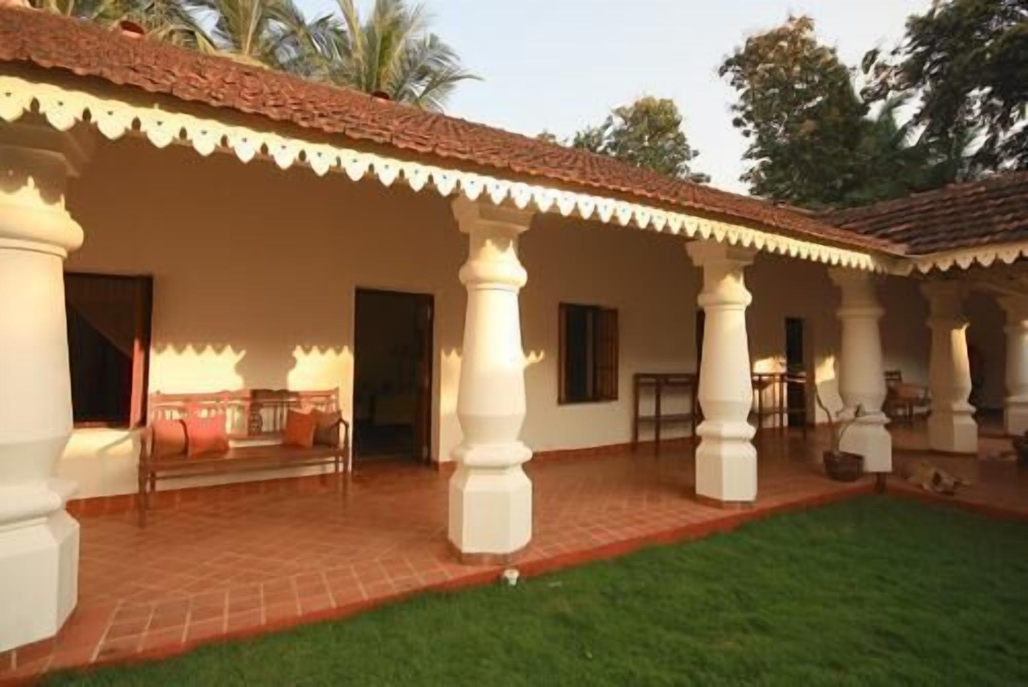A covered outdoor area with a tiled floor, white columns, and a grassy lawn.