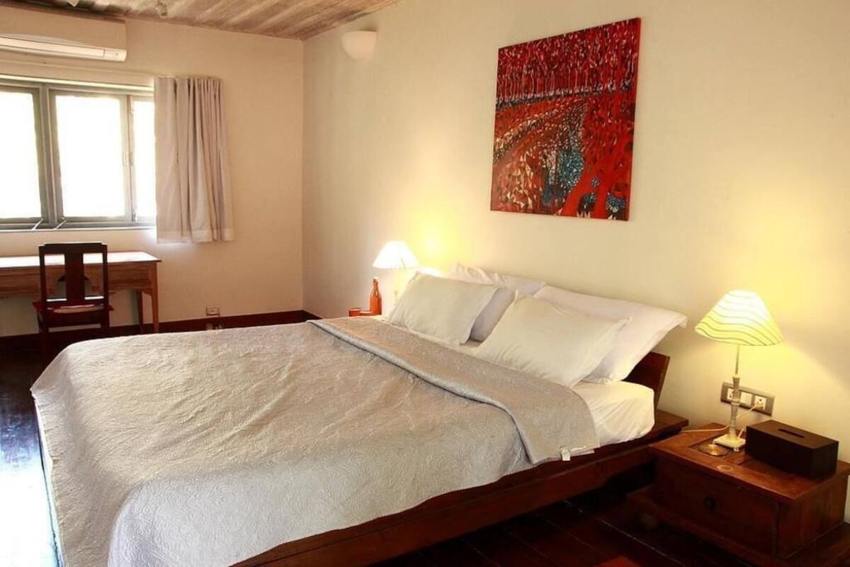 Ein Schlafzimmer mit einem Bett, Nachttischlampen, einem Schreibtisch und einem Fenster mit Vorhängen.