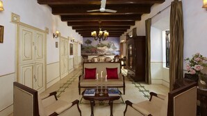 A spacious lobby with a high ceiling, a chandelier, a sofa with red cushions, and a table with books and candles. - Siolim House (Siolim)