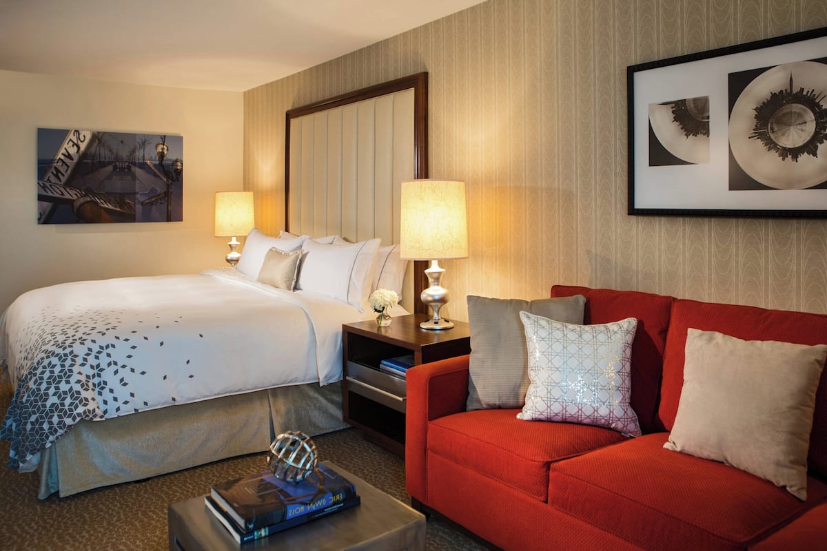 A hotel room with a large bed, a red sofa, two bedside tables with lamps, and a framed artwork on the wall.