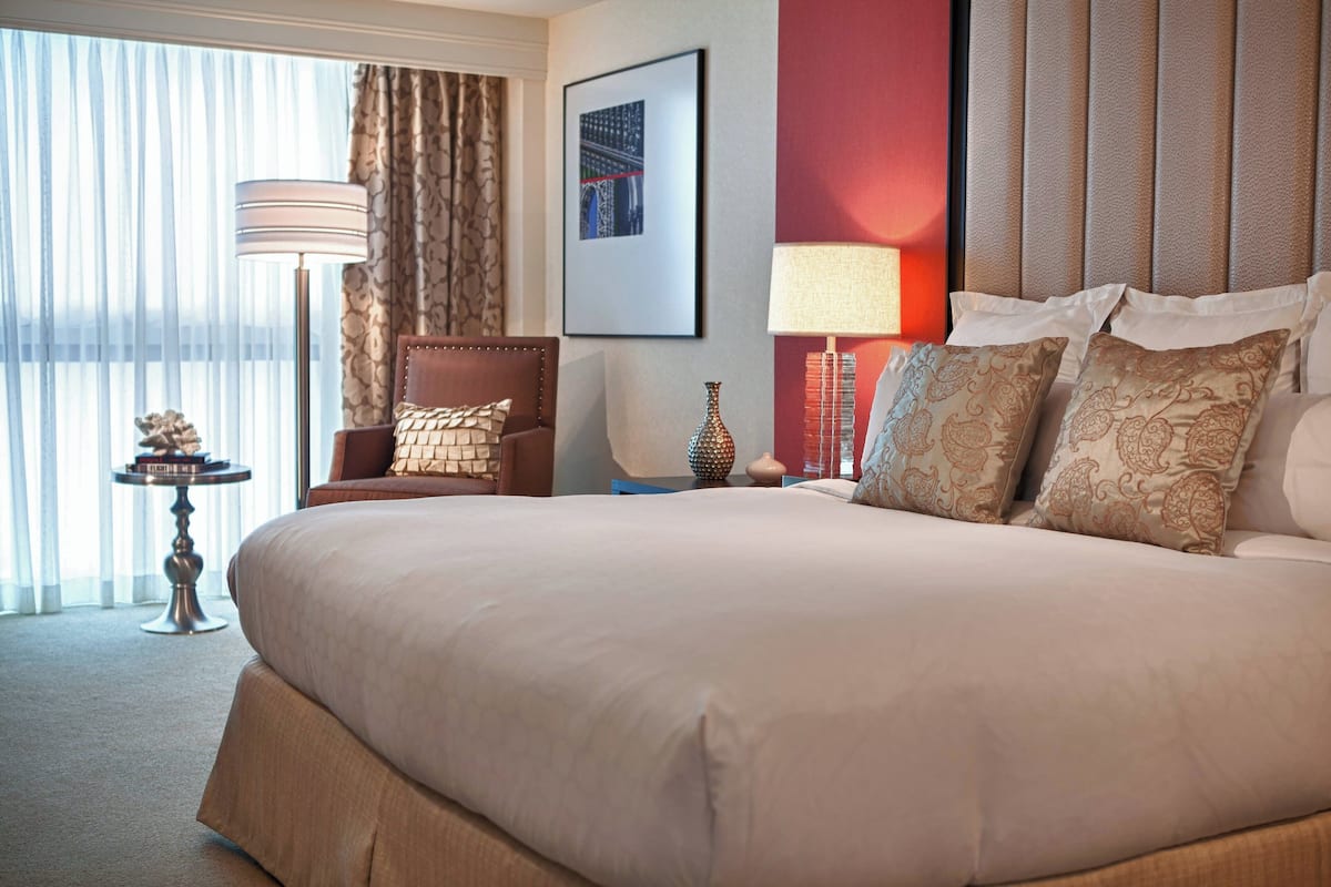 A well-appointed hotel room with a large bed, a sitting area with a chair, a lamp, and a vase on a side table.