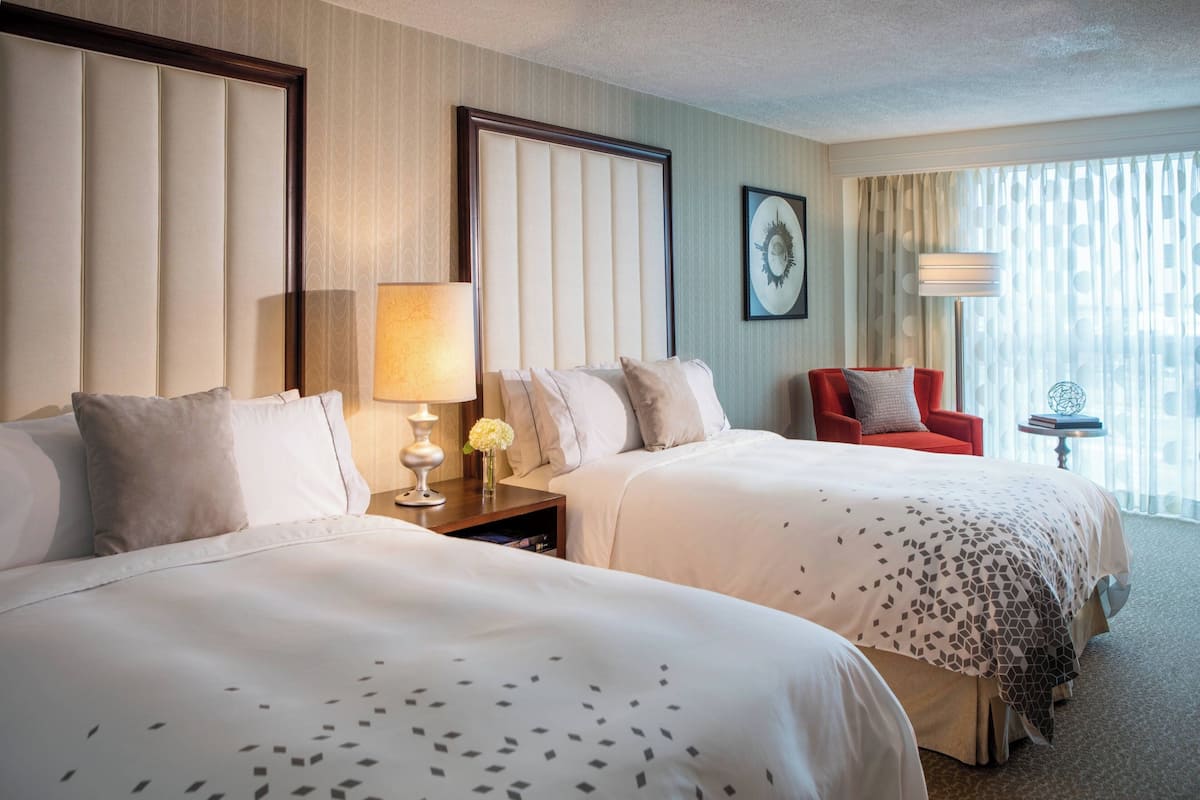 A hotel room with two beds, a red chair, a lamp, and a small table with a globe.