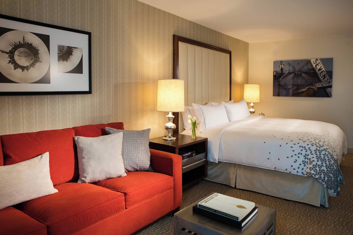 A hotel room with a red sofa, a bed with a white and blue patterned bedspread, two bedside lamps, a framed picture above the sofa, and a framed picture above the bed.