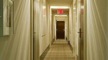 A hotel hallway with patterned carpet, doors on both sides, and a red exit sign.