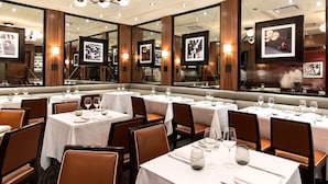 Una sala ristorante con diversi tavoli apparecchiati, ognuno con tovaglia bianca e bicchieri da vino.