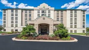 A large, multi-story hotel with a central entrance, surrounded by landscaped gardens and a clear blue sky.