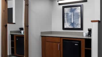 A compact bathroom with a wooden cabinet, a black refrigerator, and a framed abstract artwork on the wall.