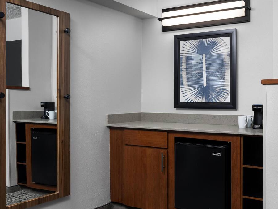 A compact bathroom with a wooden cabinet, a black refrigerator, and a framed abstract artwork on the wall.