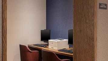 Habitación de hotel con escritorio, dos sillas, una impresora y dos monitores.