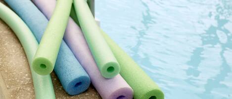 Un conjunto de rodillos de espuma de distintos colores sobre una superficie texturizada cerca de una piscina.