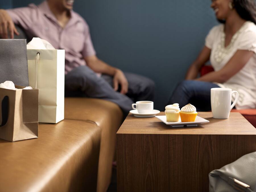 A wooden table with a cup of coffee, a muffin, and a white mug.