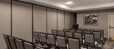 A conference room with rows of chairs, a podium, and a large painting on the wall.