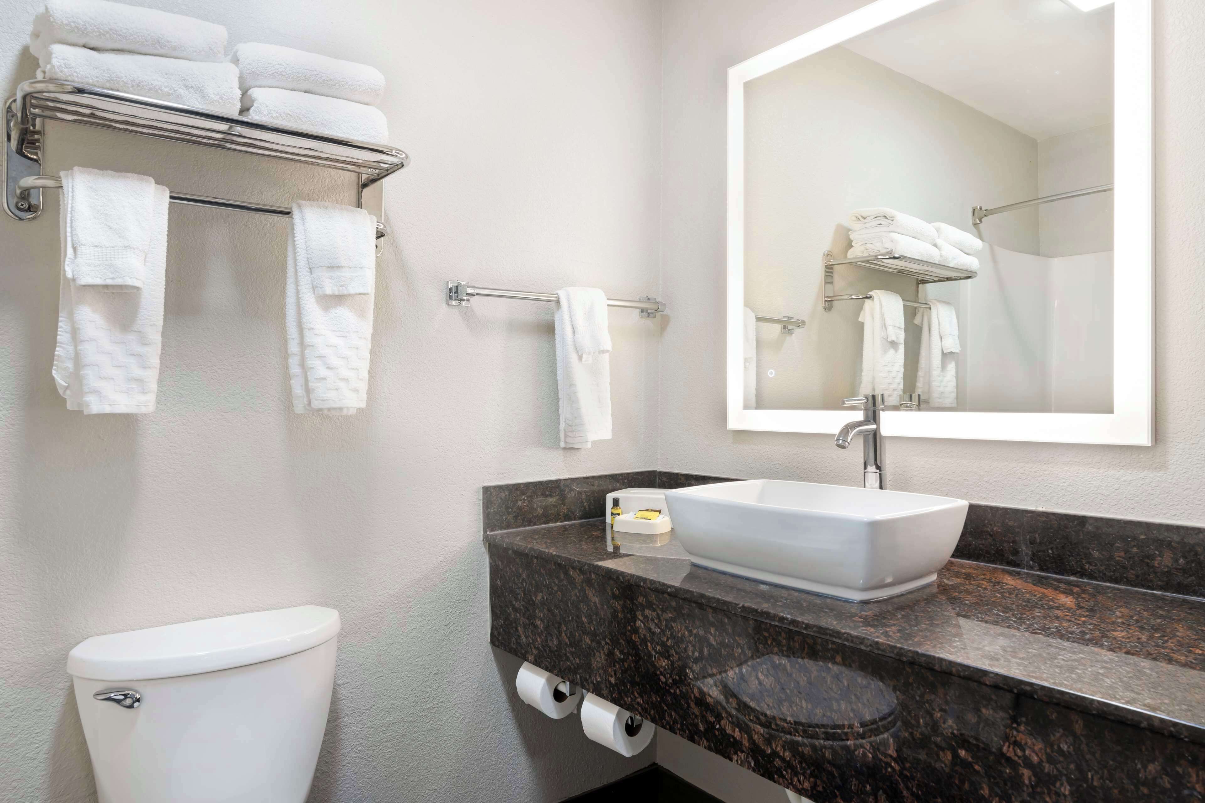 A bathroom with a white toilet, a sink with a large mirror, and a towel rack with multiple towels.