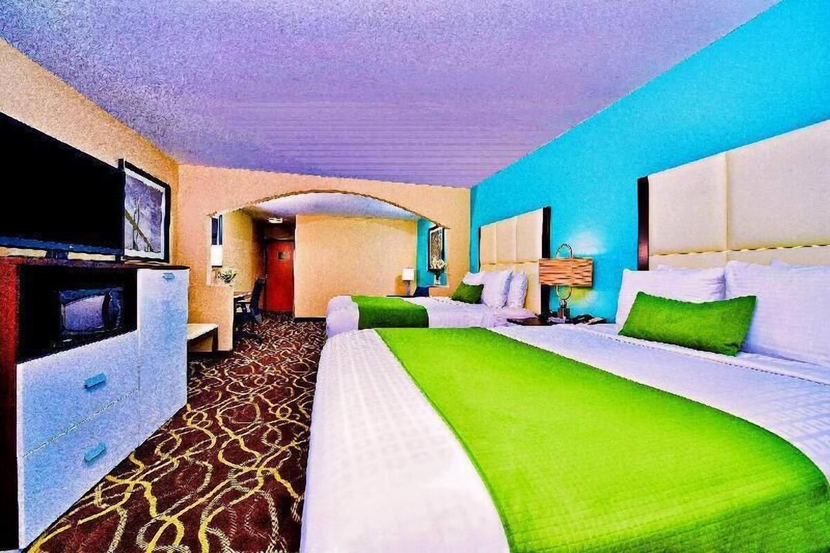 A hotel room with a large bed, a television, a desk, and a bathroom visible through an archway.