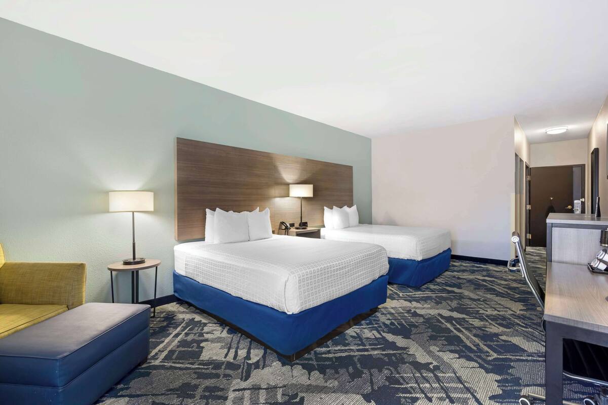 A hotel room with two beds, a desk, a chair, and a lamp.