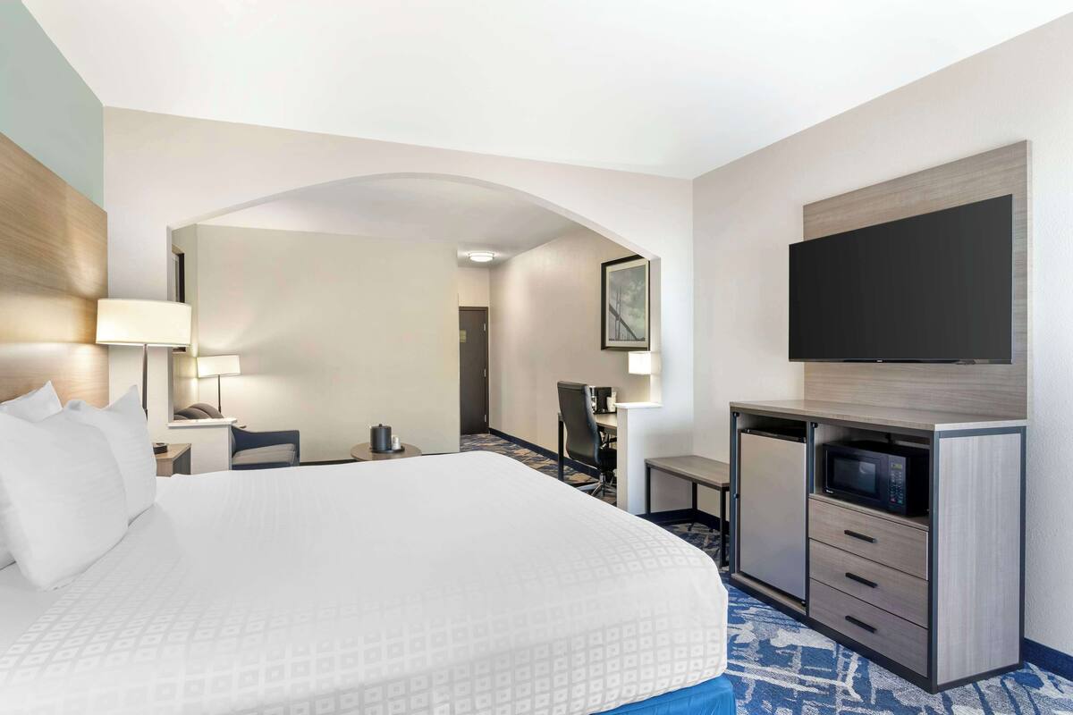 A hotel room with a large bed, a desk with a computer, a flat-screen TV, and a microwave.