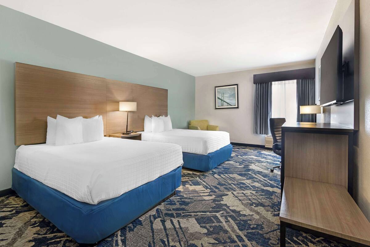 A hotel room with two beds, a desk, a chair, a TV, and a window with curtains.
