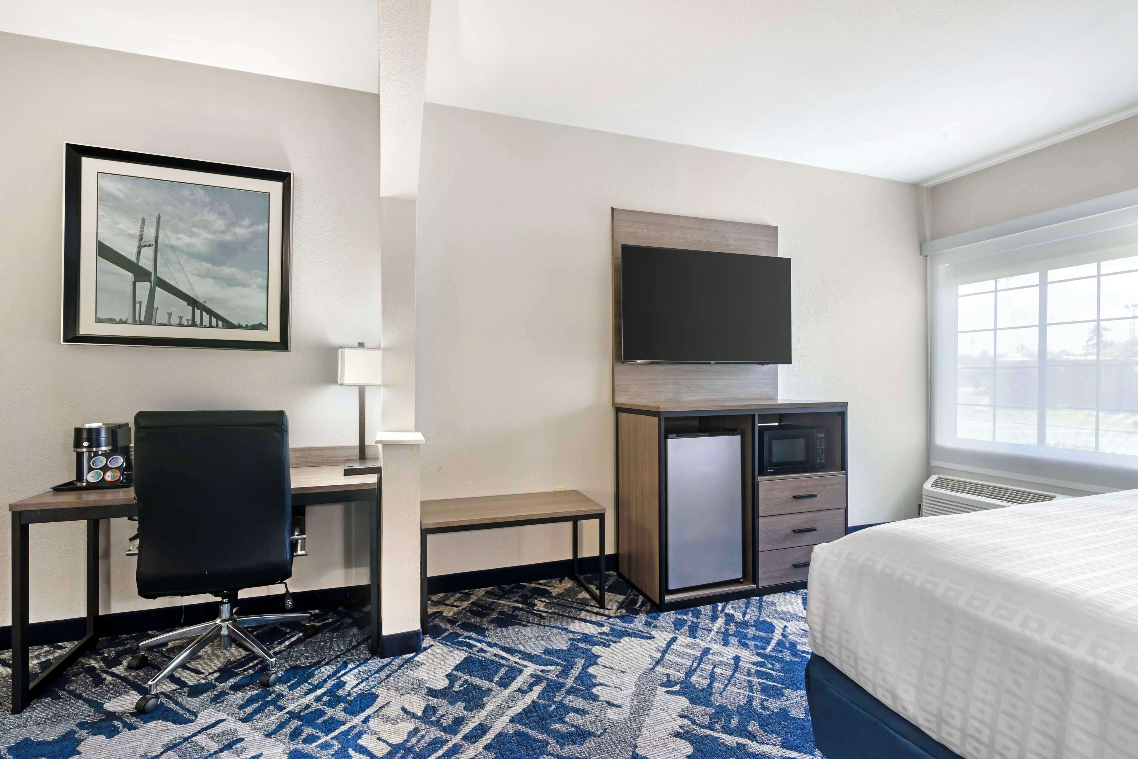 A hotel room with a bed, a desk with a chair, a television, a microwave, and a framed picture on the wall.