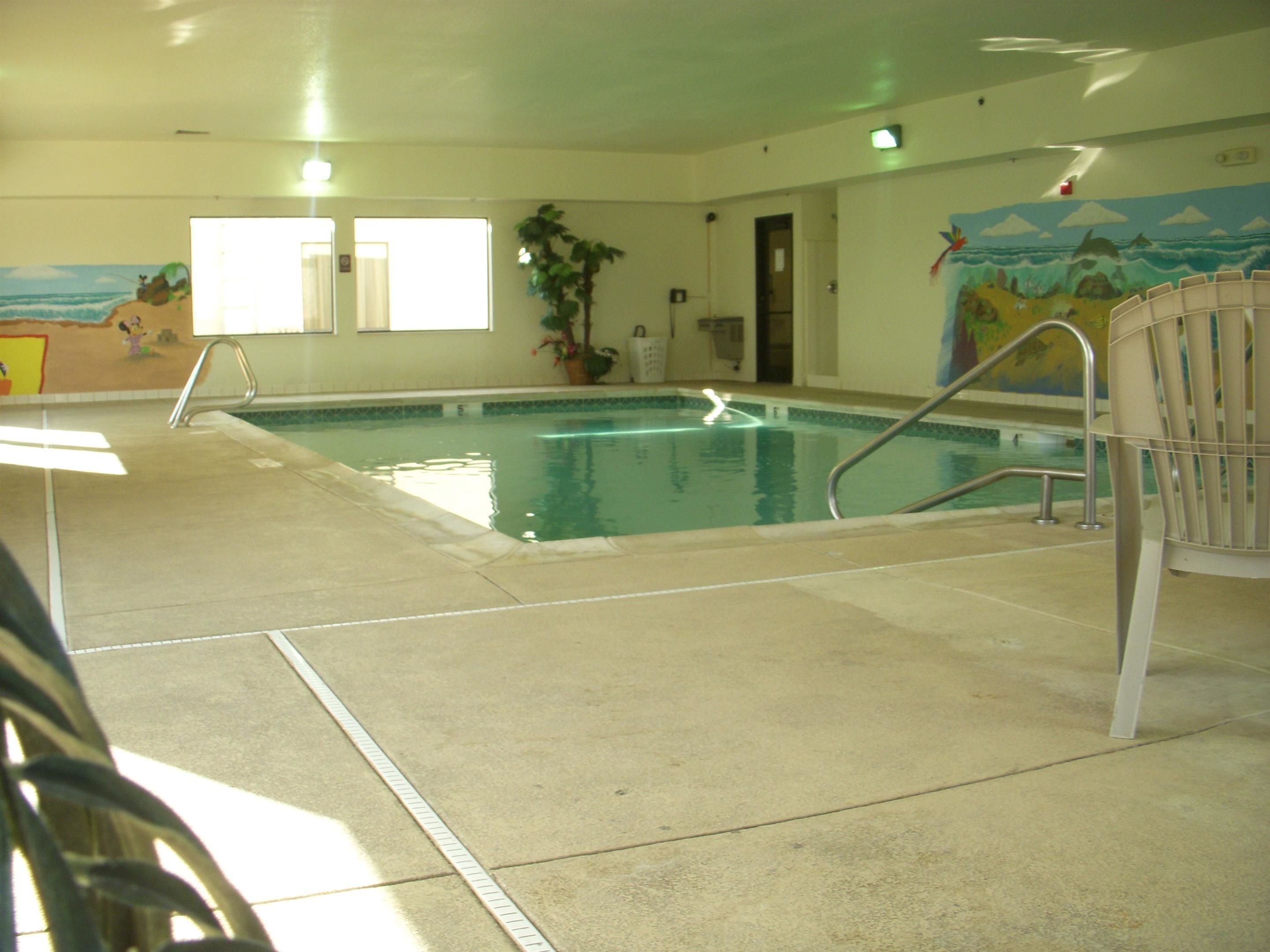 Una piscina interior con suelo de baldosas, una escalera de piscina y un mural en la pared.