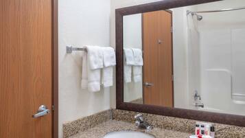 Un baño con lavamanos de encimera de granito, un espejo grande y una ducha visible al fondo.