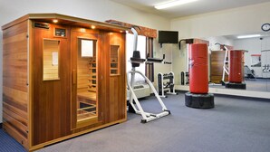 Una sauna con paredes de madera y un panel de control, una cinta de correr y sacos de boxeo rojos en un área de gimnasio.