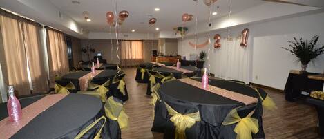 A banquet hall with tables covered in black tablecloths and yellow sashes, balloons, and a '21 years loved' decoration.