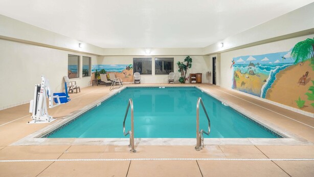 Una piscina interior con agua cristalina, rodeada de sillas de descanso y un mural que representa una playa.