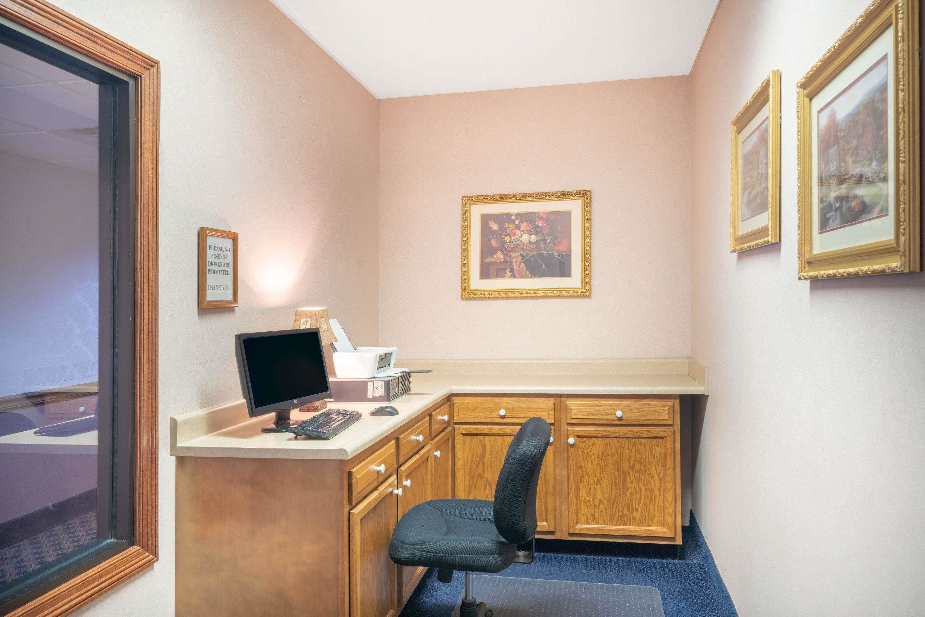 A small office with a desk, computer, and chair. There are framed pictures on the wall and a sign on the door.