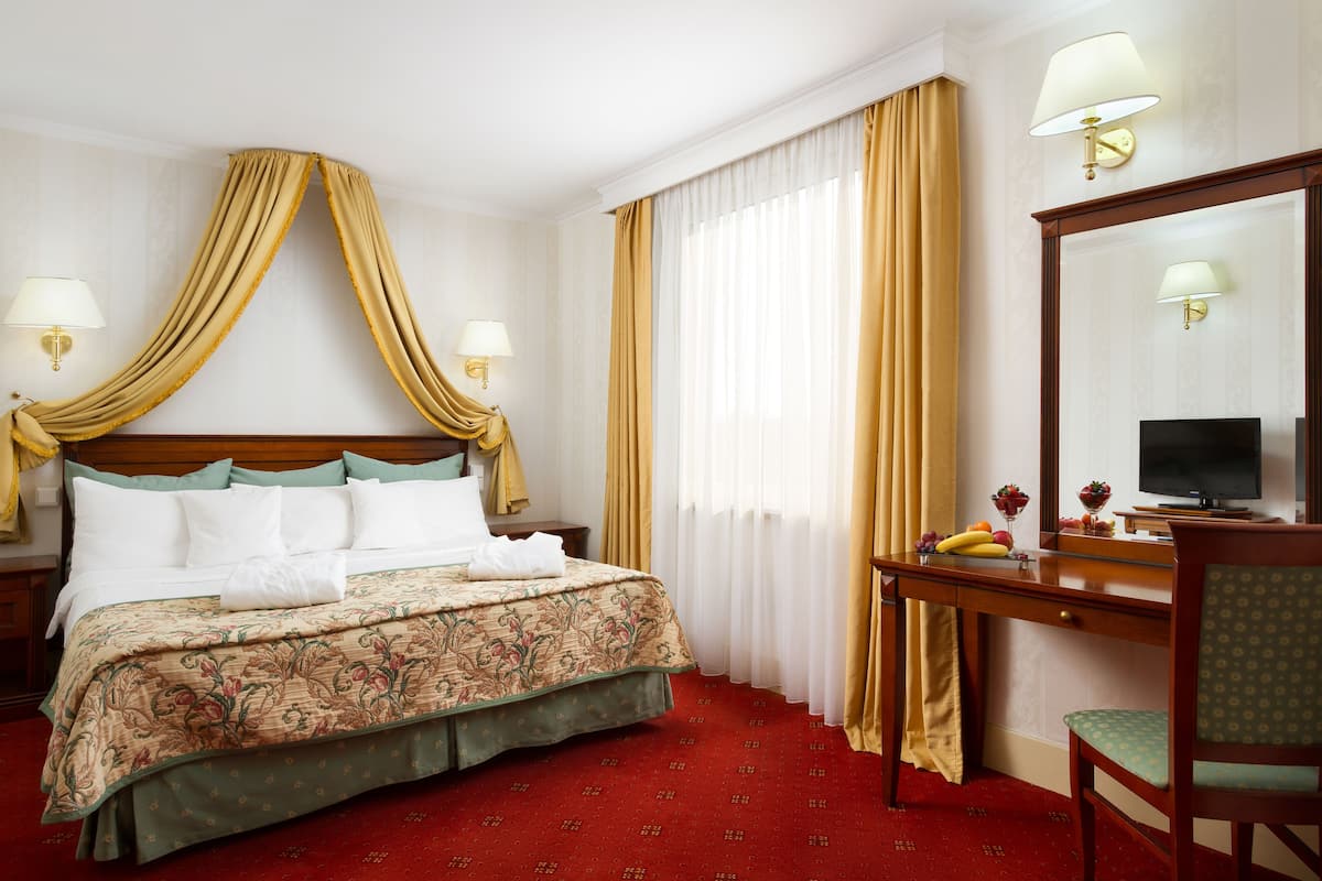 A hotel room with a bed, a desk with a computer, a chair, and a large mirror.