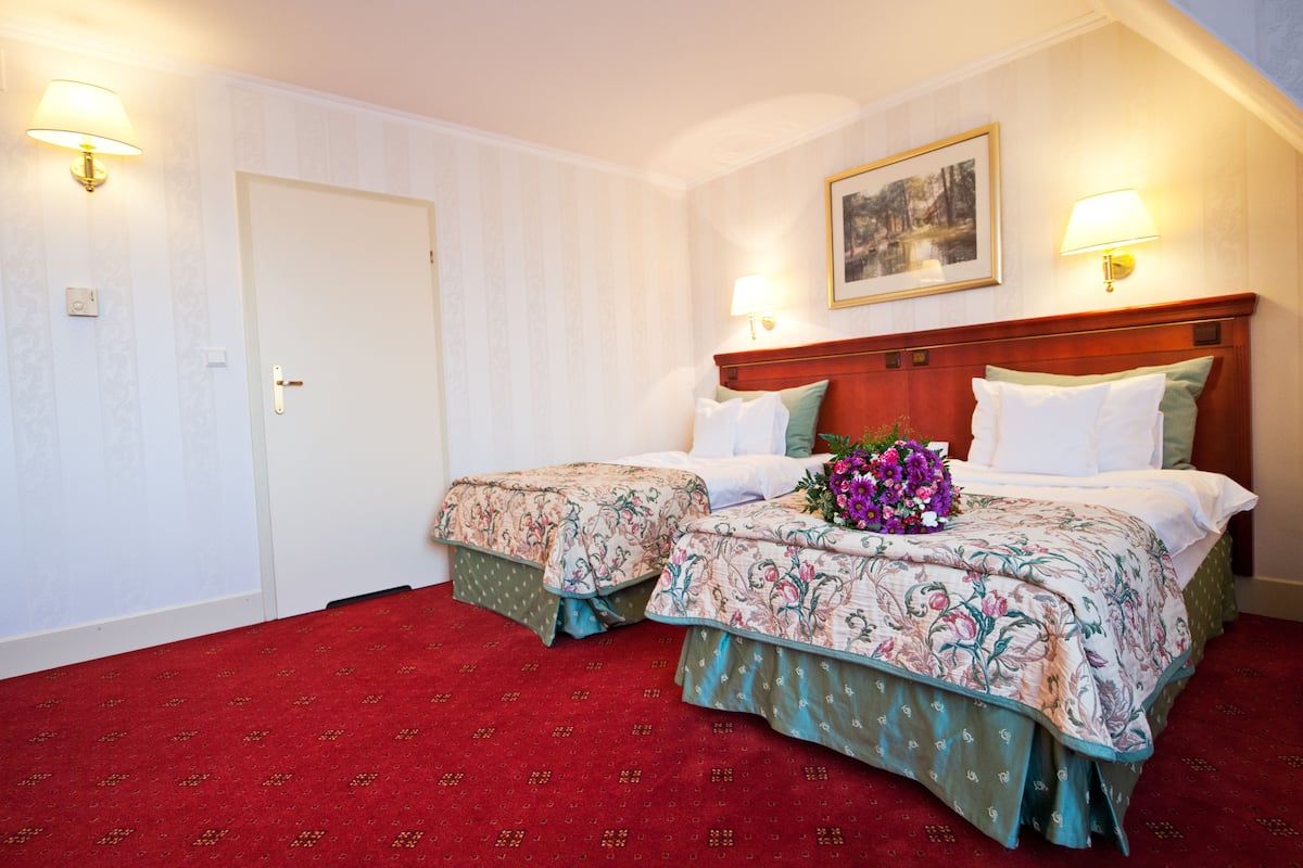 A hotel room with two beds, a red carpet, and wall-mounted lamps.