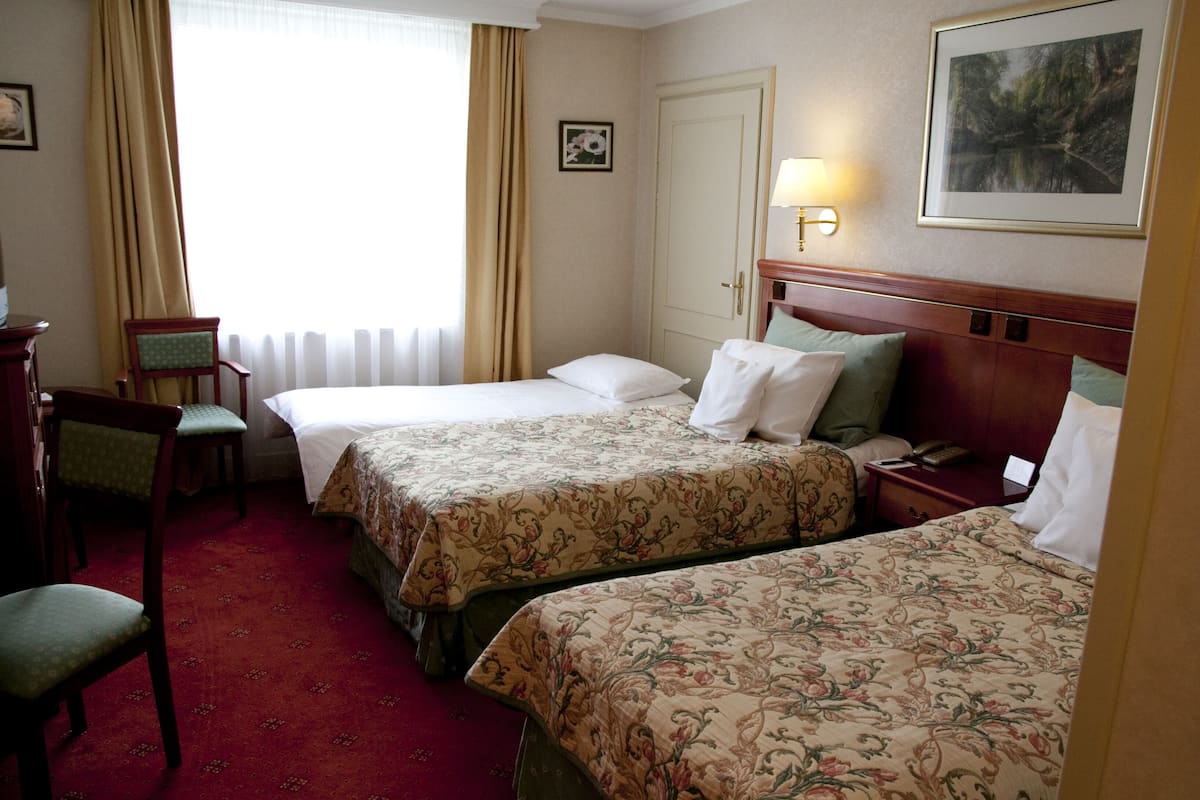 A hotel room with two beds, a desk, a chair, a lamp, and a framed picture on the wall.
