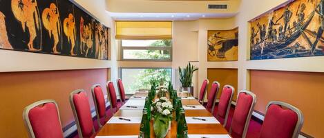 A conference room with a long table, red chairs, and artwork on the walls.