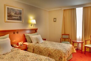 A hotel room with two beds, a nightstand with a lamp, a framed picture on the wall, and a chair by the window. - MCC Mazurkas Conference Centre & Hotel (Ozarow Mazowiecki)