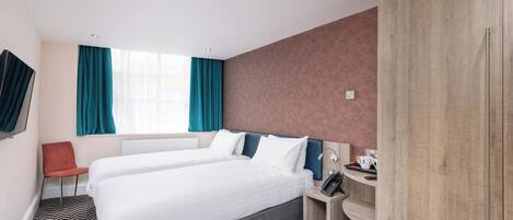 Habitación de hotel con dos camas, un escritorio con teléfono, una silla y un armario.