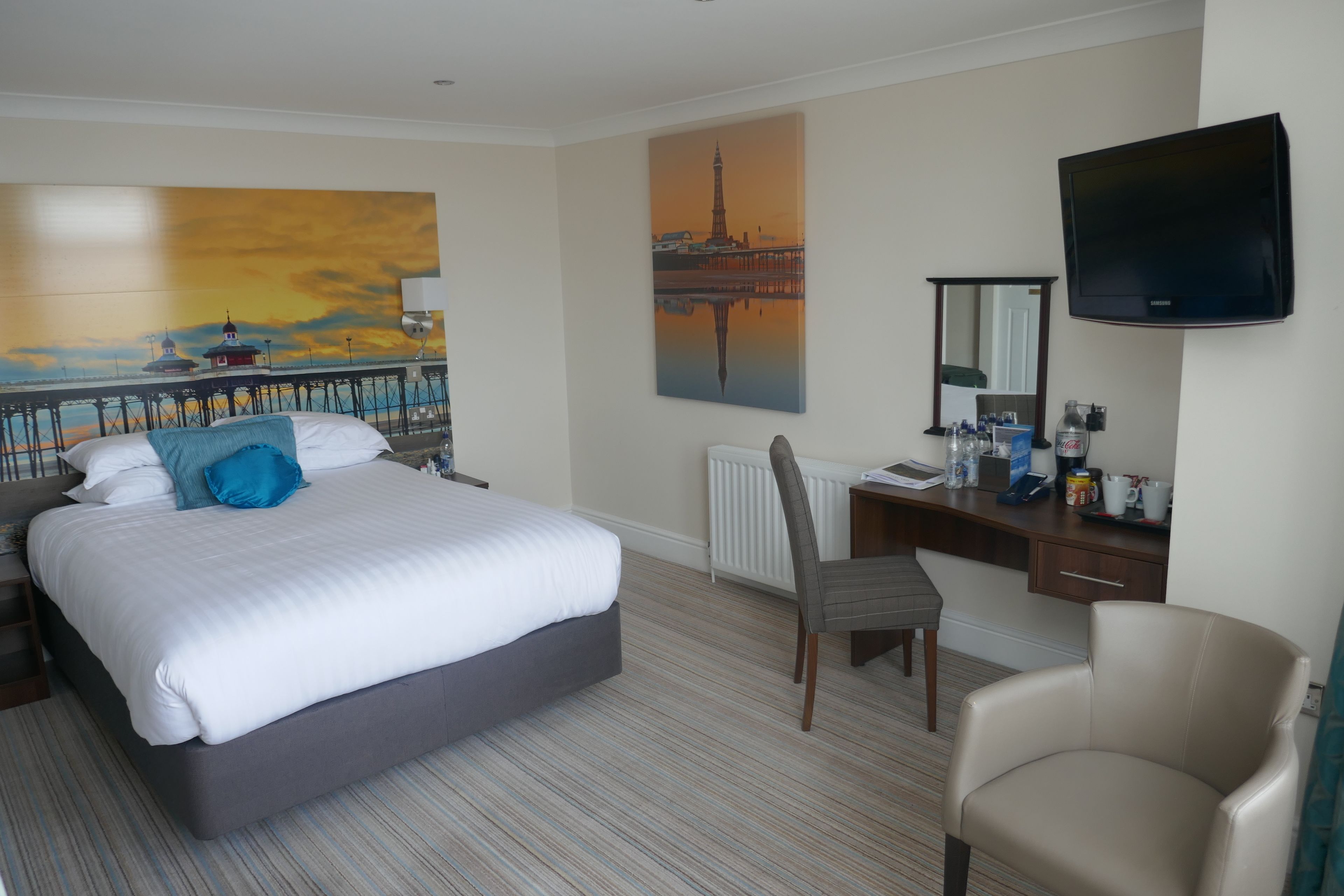 Habitación de hotel con cama, escritorio, silla, televisor y obras de arte en las paredes.