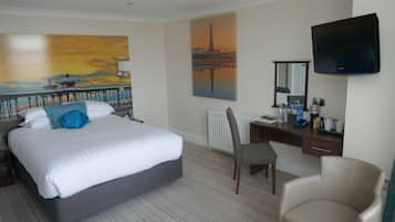 A hotel room with a bed, a desk, a chair, a television, and artwork on the walls.
