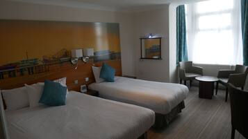 A hotel room with two beds, a small table, and a seating area.