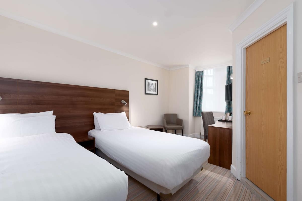 A hotel room with two beds, a wooden headboard, a small table with a chair, a television, and a door.