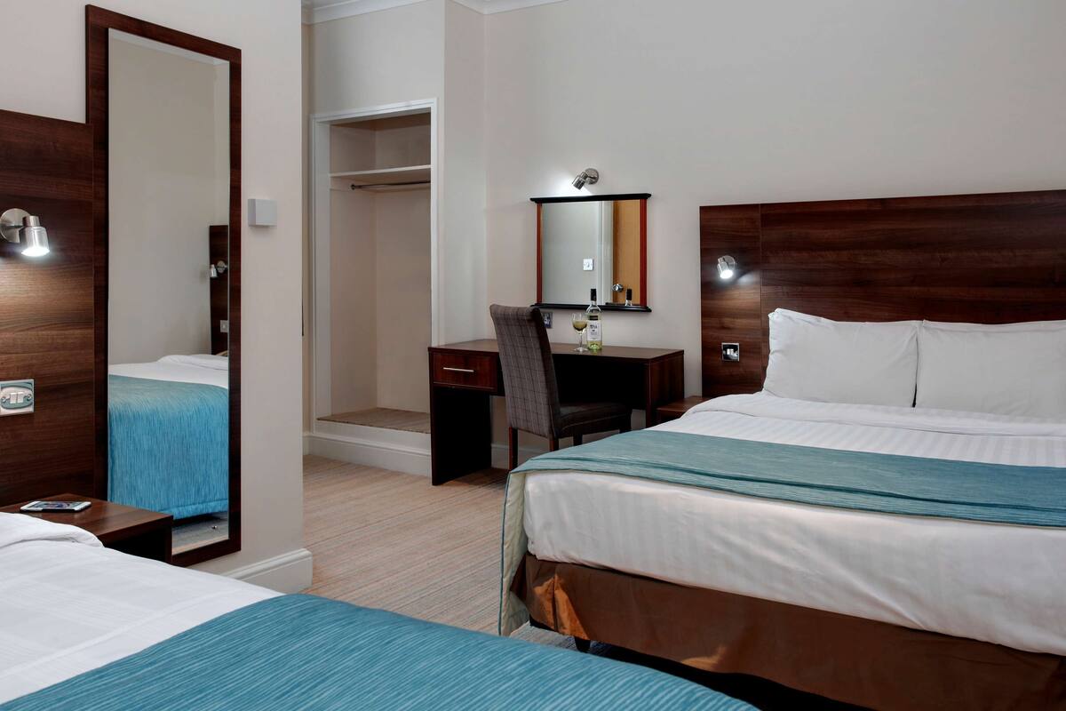 A hotel room with a bed, a desk, a chair, a mirror, and a wardrobe.