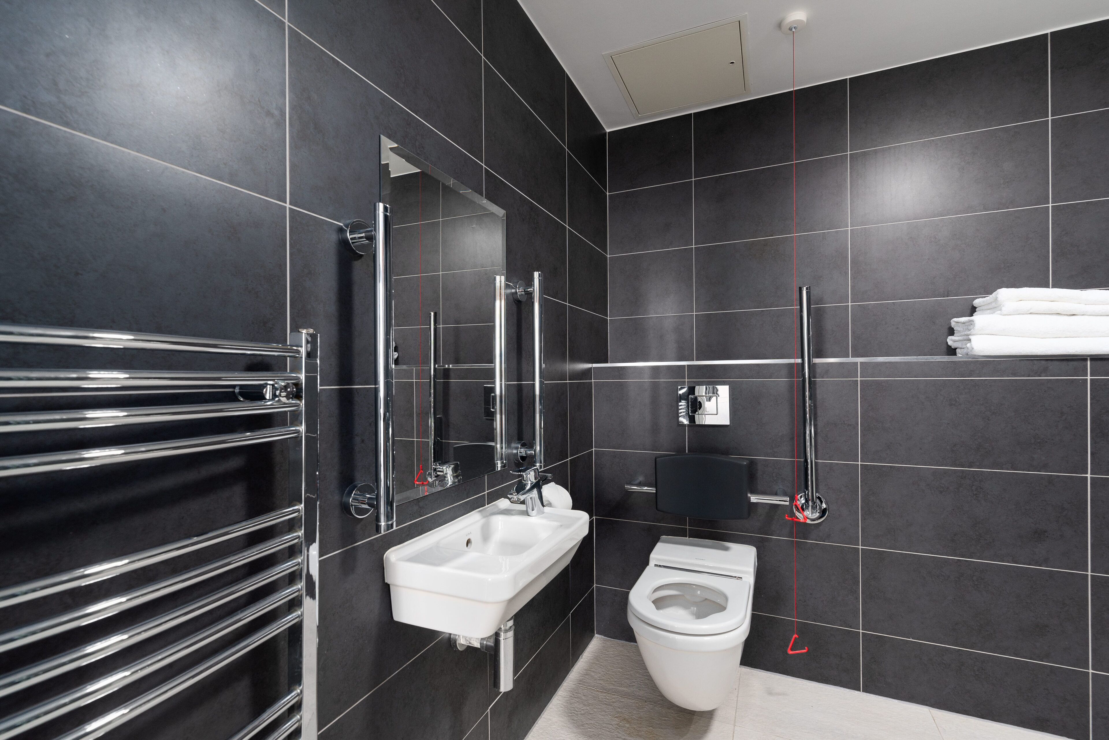 Un baño moderno con lavamanos blanco, toallero cromado y retrete.