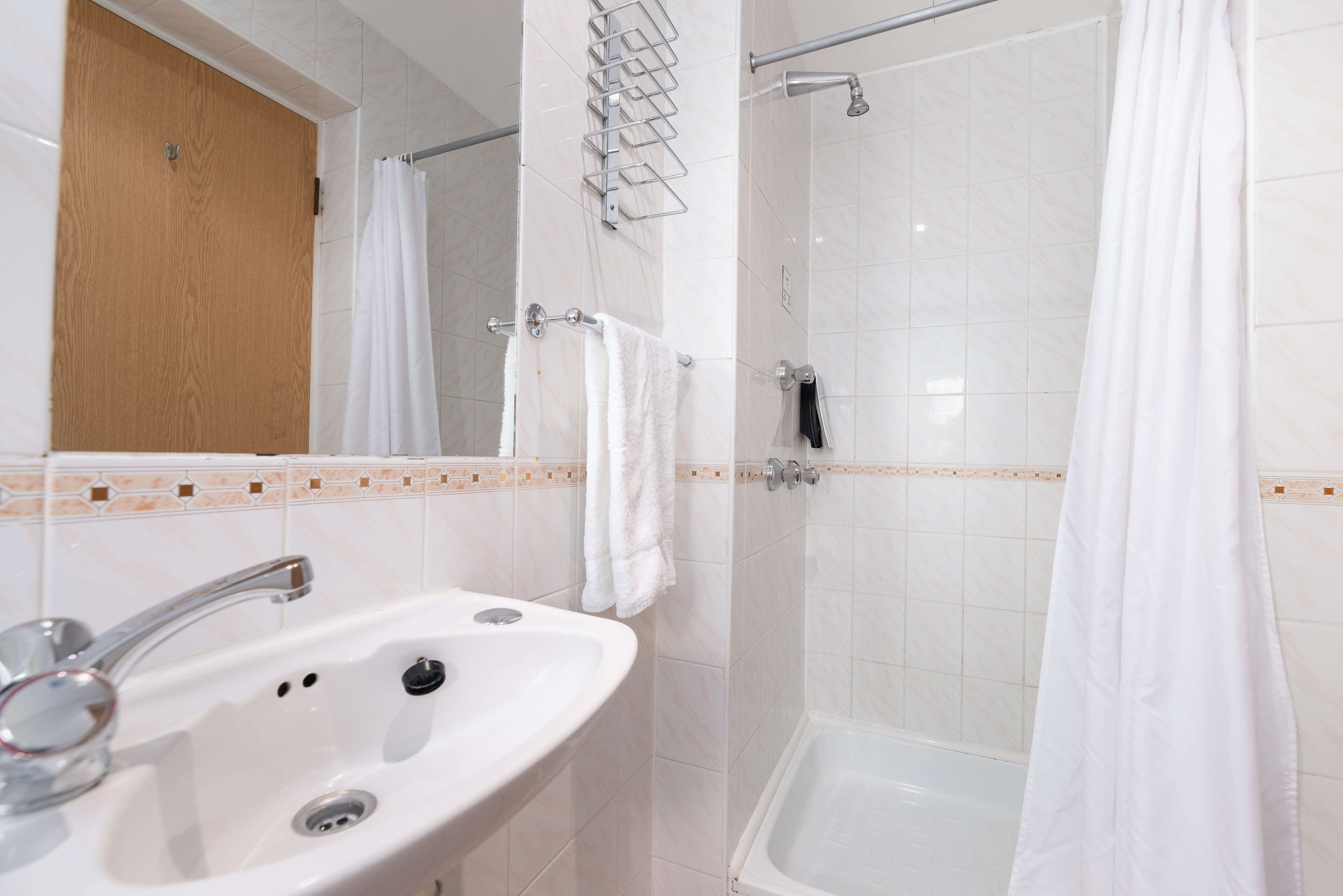 Une salle de bain équipée d’un lavabo, d’un miroir, d’une douche et d’un porte-serviettes.