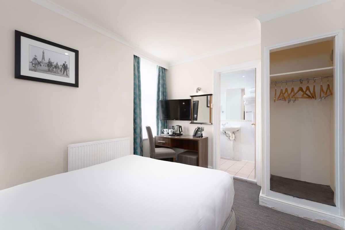 A hotel room with a bed, a desk with a chair, a television, a framed picture on the wall, and a walk-in closet.
